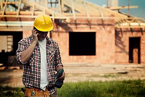 ouvrier en chemise à carreaux qui téléphone avec une maison en brique en construction an arrière plan